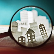 Magnifying glass in front of an open newspaper with paper houses. Concept of rent, search, purchase real estate.