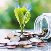 Plant growing from coins outside the glass jar on blurred green natural background for business and financial growth concept