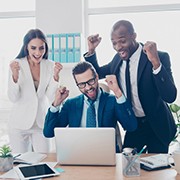 Three cheerful, full of happiness, professional, lucky experts celebrating a victory, income growth of their company, having raised arms, looking at screen of computer in workplace