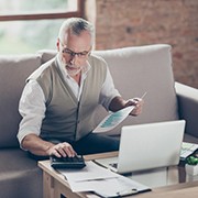 Old confident clever concentrated bearded grandpa is checking his calculations sitting in front of monitor at office